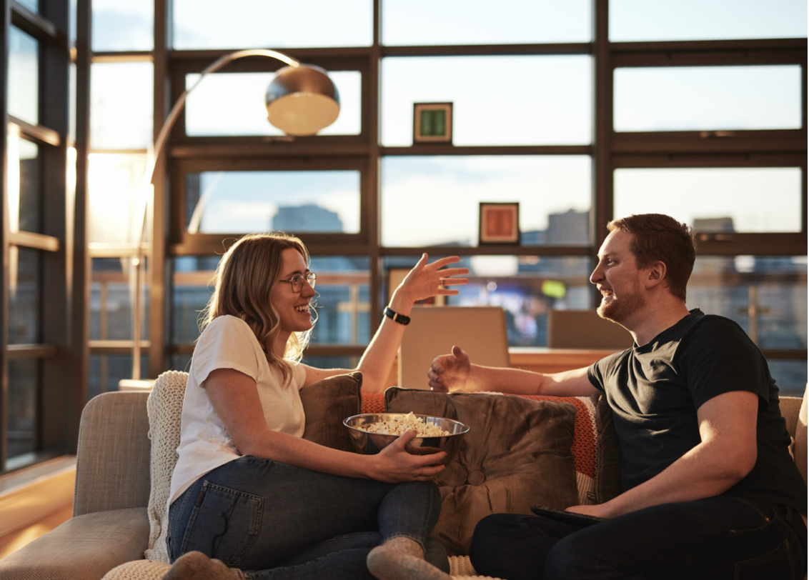 Ehepaar sitzt lachend mit Popcorn auf dem Sofa